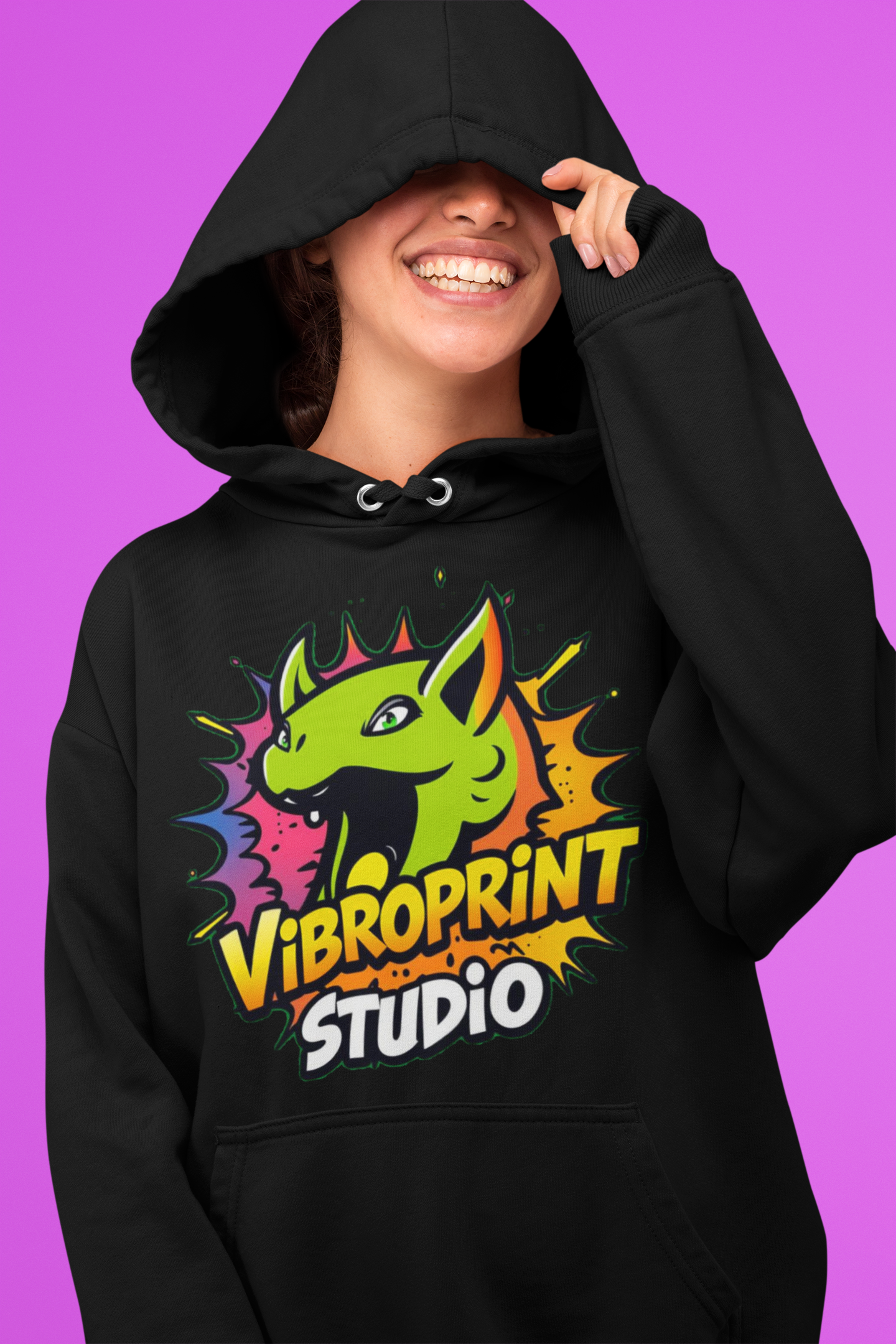 Smiling woman wearing a black hoodie featuring the bright and colorful dragon design of Vibroprint Studio, set against a vibrant pink background.