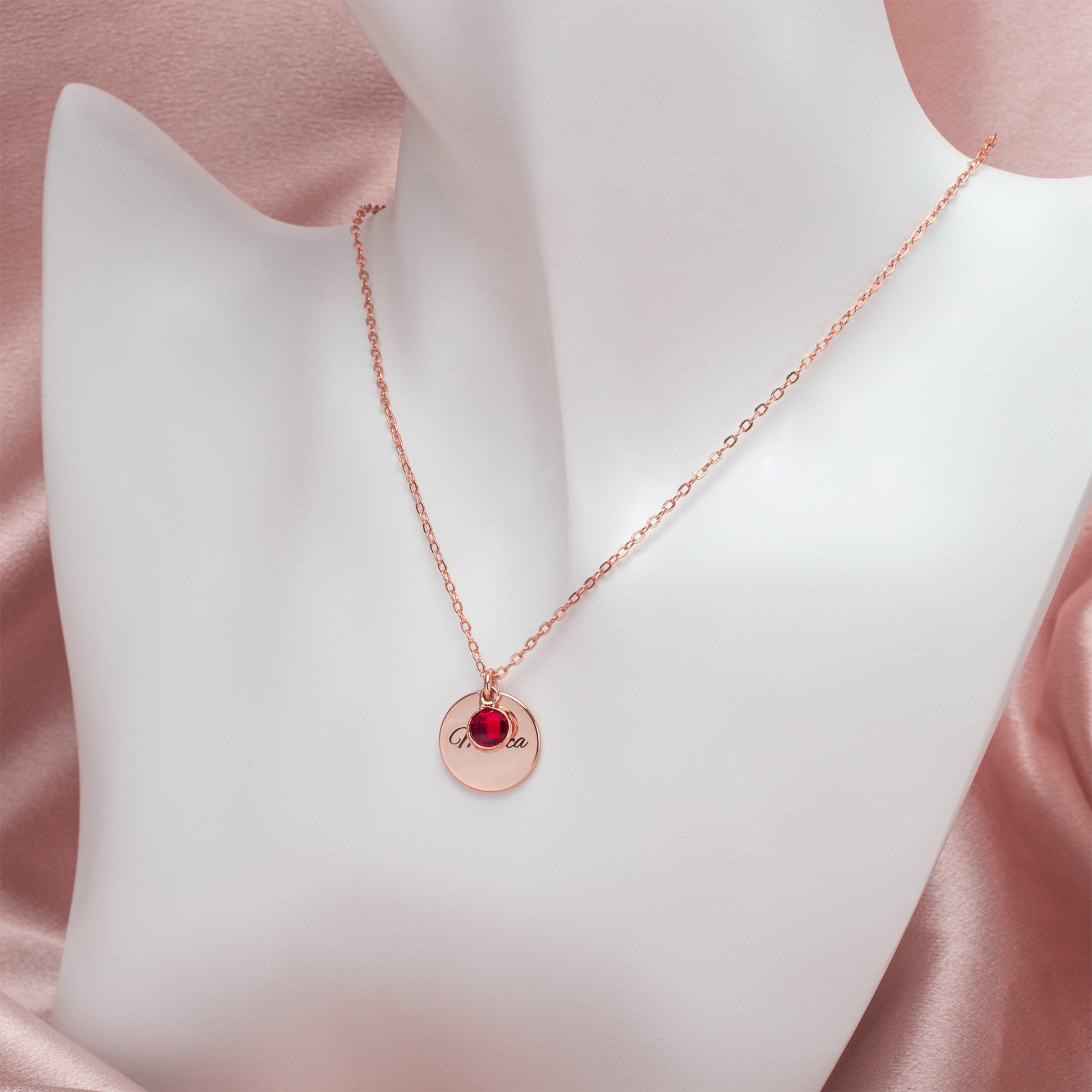 Model wearing a personalized copper circle necklace with a July ruby birthstone. Gift box shown in the background. (Showcases the necklace on a model and subtly mentions the gift box)