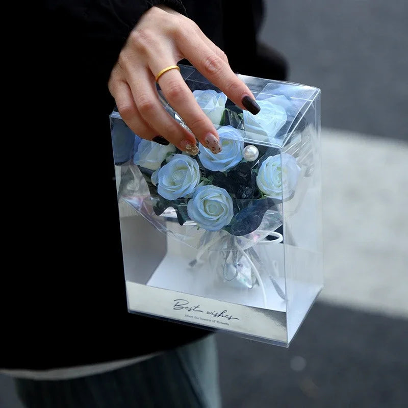 Three red artificial soap roses nestled in a white gift box with a clear lid