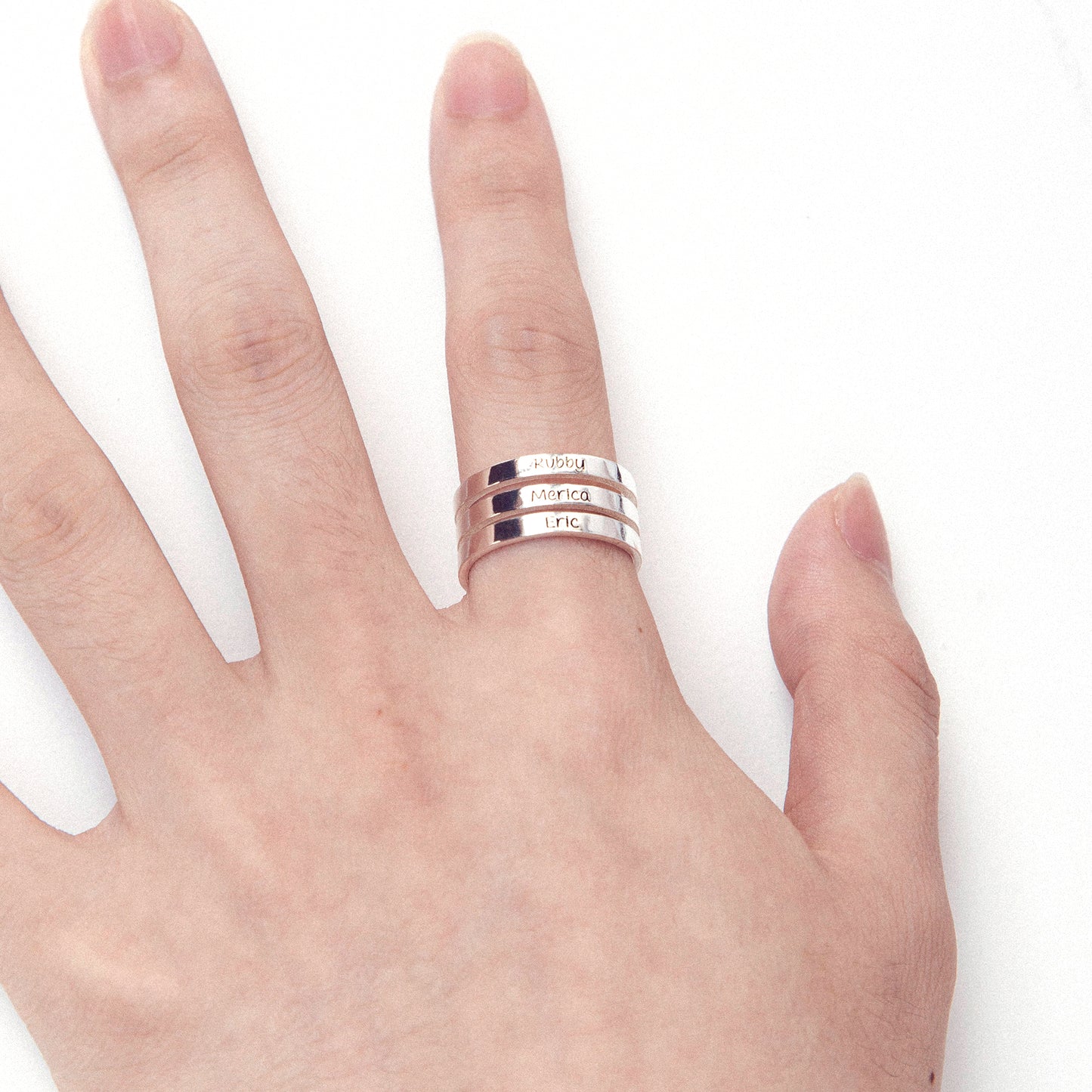 Hand holding a personalized sterling silver stackable name ring engraved with "John," demonstrating its size and shine. (Provides context with the hand and focuses on specific engraving while mentioning visual qualities)